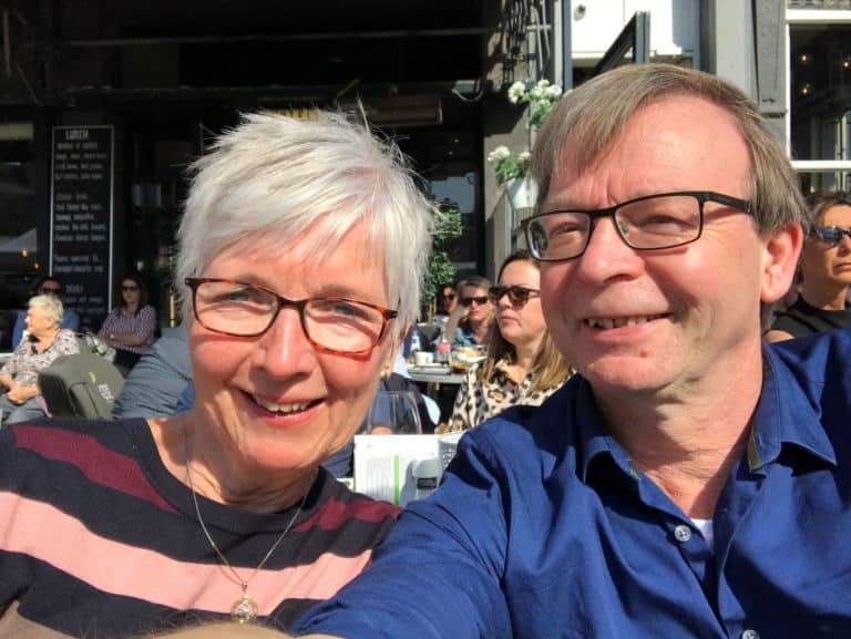 Robert & Nelly 1 Een man en een vrouw met een hoog EQ omhelzen elkaar buiten, de ogen gesloten, terwijl de man zachtjes haar voorhoofd kust in een gebaar van troost en genegenheid. Beiden dragen blauw en zien er kalm en vredig uit tegen een achtergrond van groen.
