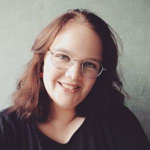 Nathalie & Hugo 1 Een man en een vrouw met een hoog EQ omhelzen elkaar buiten, de ogen gesloten, terwijl de man zachtjes haar voorhoofd kust in een gebaar van troost en genegenheid. Beiden dragen blauw en zien er kalm en vredig uit tegen een achtergrond van groen.