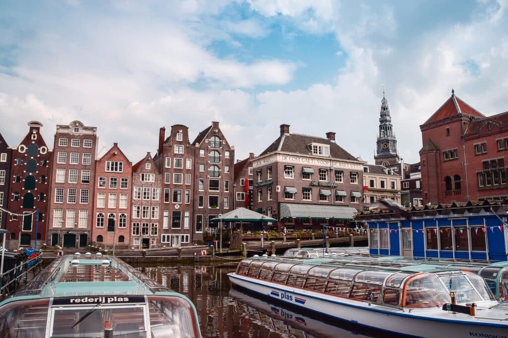 Een gracht in Amsterdam met rondvaartboten met glazen daken aangemeerd voor traditionele Nederlandse gebouwen - een ideale partner om de smalle gevels, zadeldaken en de kerktoren die oprijst onder een gedeeltelijk bewolkte hemel te verkennen.