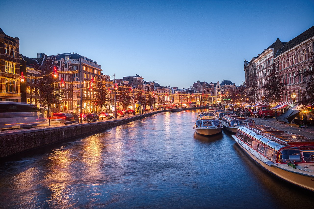 Een schilderachtig uitzicht op een Amsterdamse gracht in de schemering, met verlichte gebouwen en boten aangemeerd langs het water-een levendig tafereel perfect voor een avondwandeling met je ideale partner als de stadslichten weerspiegelen op de kalme gracht. Een schilderachtig uitzicht op een Amsterdamse gracht in de schemering, met verlichte gebouwen en boten aangemeerd langs het water-een levendig tafereel perfect voor een avondwandeling met je ideale partner als de stadslichten weerspiegelen op de kalme gracht.