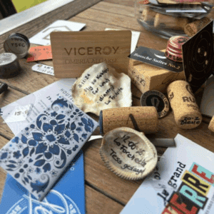 Een tafel bezaaid met wijnkurken, visitekaartjes, handgeschreven notities, een kaart met blauw patroon, een houten bord "Viceroy Ombria Algarve", doppen van PartnerSelect-flessen en verschillende promotieartikelen.