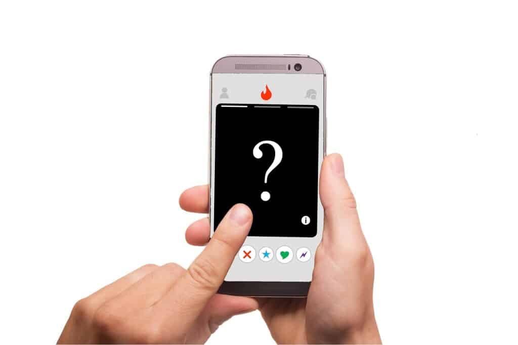 De handen van een persoon die een smartphone vasthoudt met een datingapp-profiel met een groot vraagteken in het fotogebied en zichtbare veegopties eronder, op zoek naar de ideale partner.