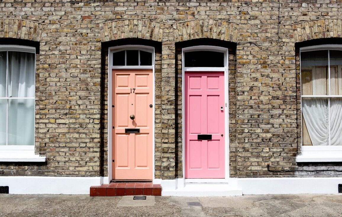 Twee naburige bakstenen rijtjeshuizen, perfect voor LAT-wonen, hebben gewelfde ramen en twee voordeuren – een perzikkleurig met het nummer 17, de andere roze – elk geaccentueerd door kraakheldere witte sierlijsten rond de deuren en ramen. Twee naburige bakstenen rijtjeshuizen, perfect voor LAT-wonen, hebben gewelfde ramen en twee voordeuren - een perzikkleurig met het nummer 17, de andere roze - elk geaccentueerd door kraakheldere witte sierlijsten rond de deuren en ramen.