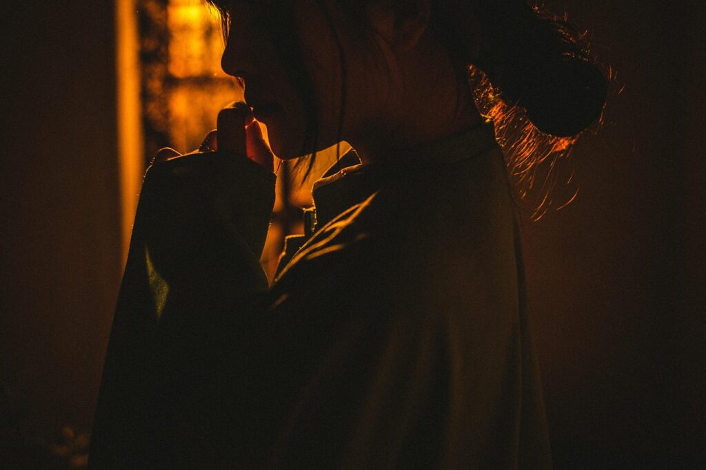 Een persoon in een los gewaad wordt getoond in warm, laag licht met het gezicht meestal in de schaduw, de hand naar de mond brengend en onzeker in een relatie lijkend - nadenkend of contemplatief.