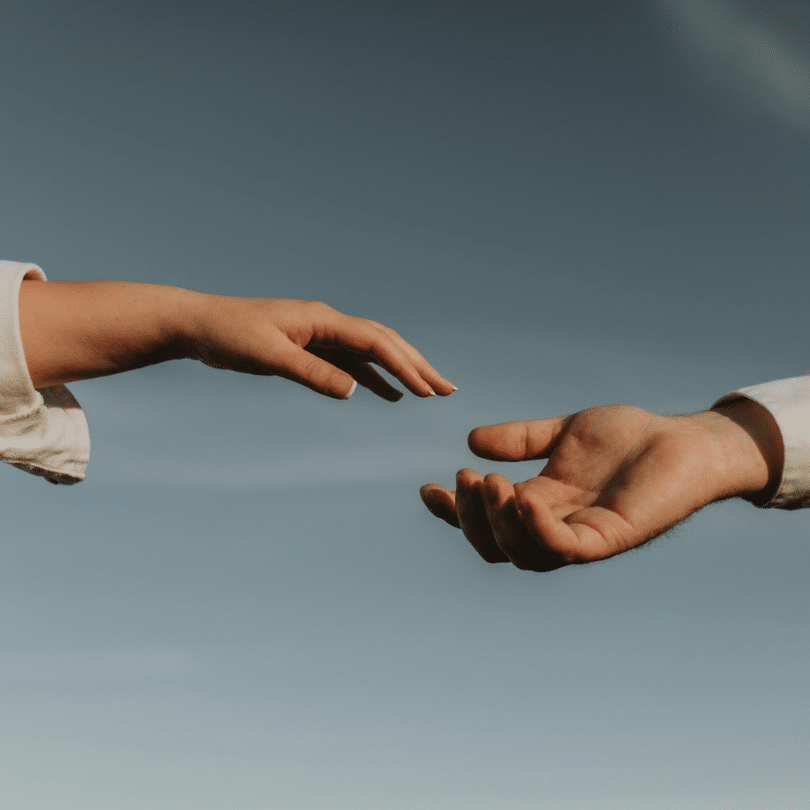 Twee handen, een vrouwelijke en een mannelijke, beide in een shirt met lange mouwen, reiken naar elkaar toe tegen een heldere hemel - de vingers raken elkaar bijna - een moment van verbinding geïnspireerd door de PartnerSelect ervaring.