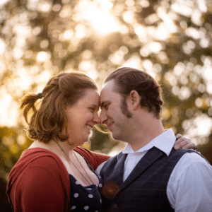 Een stel staat dicht tegen elkaar aan bij zonsondergang, raakt elkaars voorhoofd aan en glimlacht hartelijk naar elkaar als echte tegenpolen, met zacht zonlicht en vage bomen op de achtergrond.