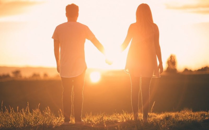 Een paar staat hand in hand, met uitzicht op een heldere zonsondergang in een open veld. Hun silhouetten gloeien in het warme licht en roepen hoop en genezing op na een relatie met een narcist, in een vredige en romantische sfeer.