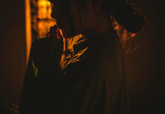 Een persoon in een los gewaad wordt getoond in warm, laag licht met het gezicht meestal in de schaduw, de hand naar de mond brengend en onzeker in een relatie lijkend - nadenkend of contemplatief.