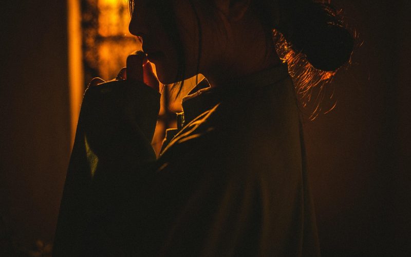 Een persoon in een los gewaad wordt getoond in warm, laag licht met het gezicht meestal in de schaduw, de hand naar de mond brengend en onzeker in een relatie lijkend - nadenkend of contemplatief.